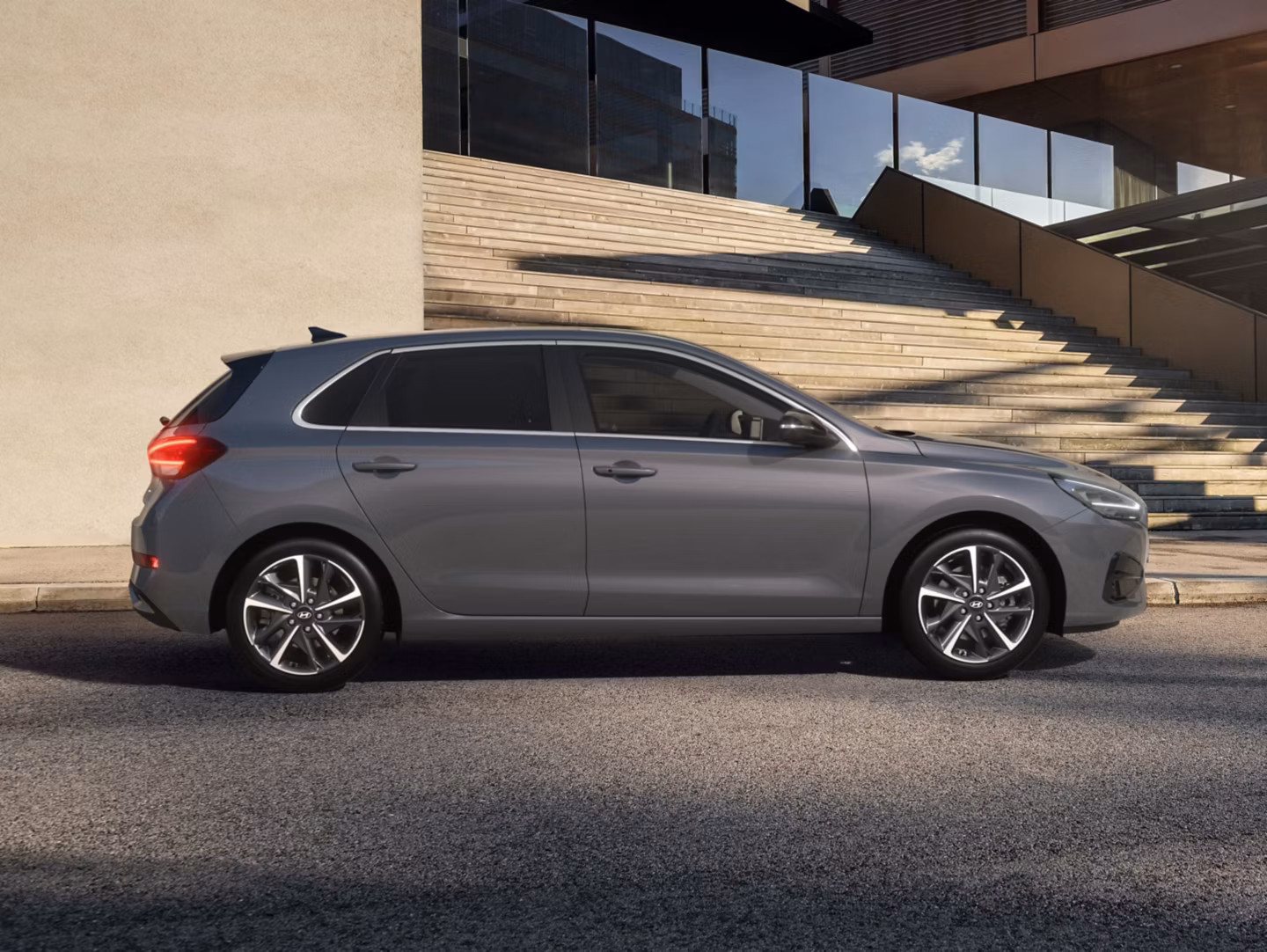 Side view of the new Hyundai i30 in grey, parked outside a wide, open staircase.